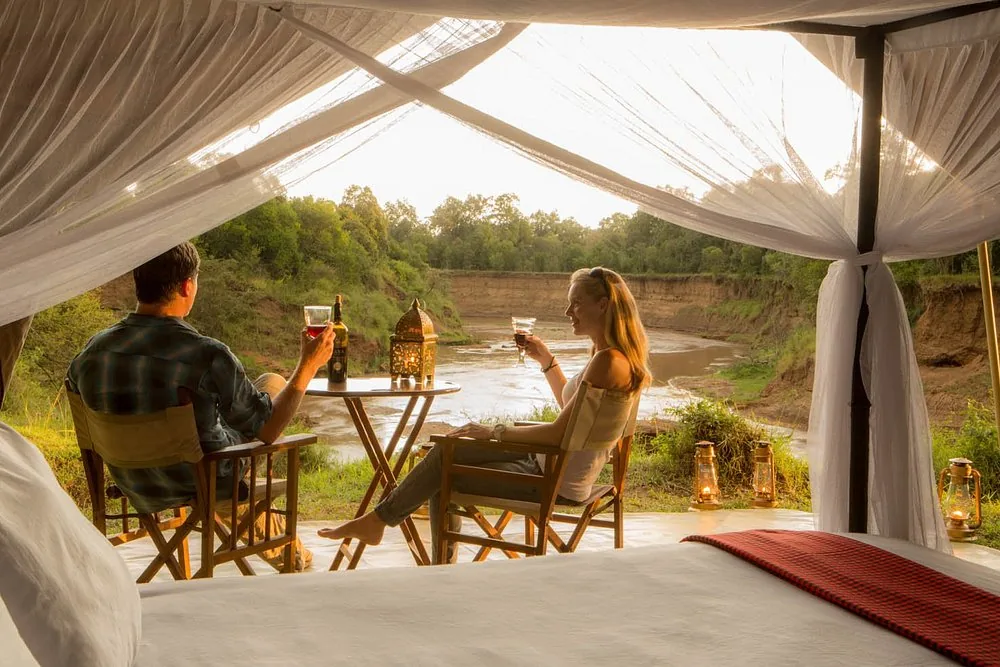 Guests on a tented camp deck above a river at sunset
